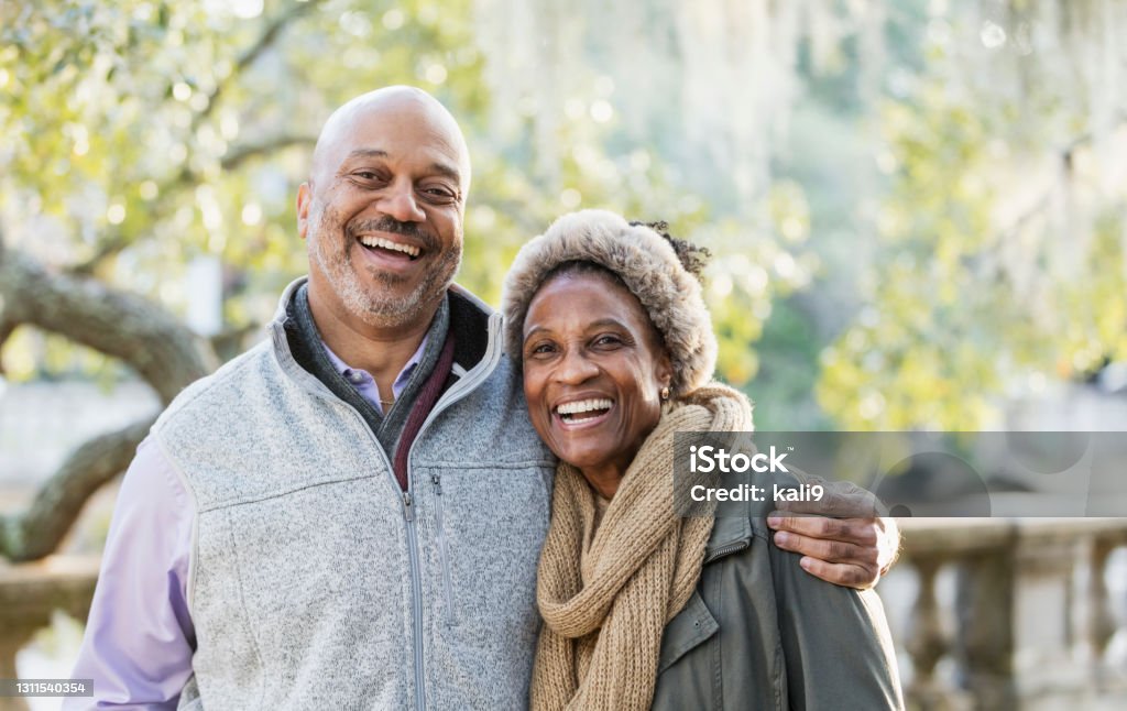 Mature African-American couple at the park Headshot of a mature African-American couple taking a walk in the park on a sunny fall day. The man is in his 50s, and his wife is a senior, in her 60s. They are standing together, smiling at the camera. Senior Couple Stock Photo
