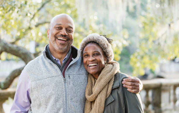 Mature African-American couple at the park Headshot of a mature African-American couple taking a walk in the park on a sunny fall day. The man is in his 50s, and his wife is a senior, in her 60s. They are standing together, smiling at the camera. side by side stock pictures, royalty-free photos & images