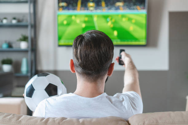 istock Casually dressed man spending his day-off at home sitting on sofa watching soccer play live braodcast on tv and supporting his favourite team 1311541420