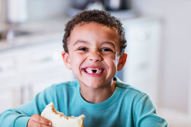 Mixed race boy eating peanut butter sandwich Close-up of the face of a cute little boy eating a peanut butter sandwich at home in the kitchen. He is 5 years old, mixed race African-American and Caucasian. He is grinning at the camera, missing his front teeth. gap toothed photos stock pictures, royalty-free photos & images