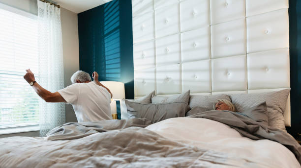 starszy mężczyzna wstać z łóżka, żona wciąż śpi - sleeping lying on back couple bed zdjęcia i obrazy z banku zdjęć