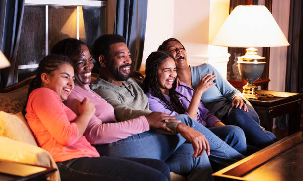 familia afroamericana con tres hijas viendo la televisión - women sofa teenage girls hairstyle fotografías e imágenes de stock