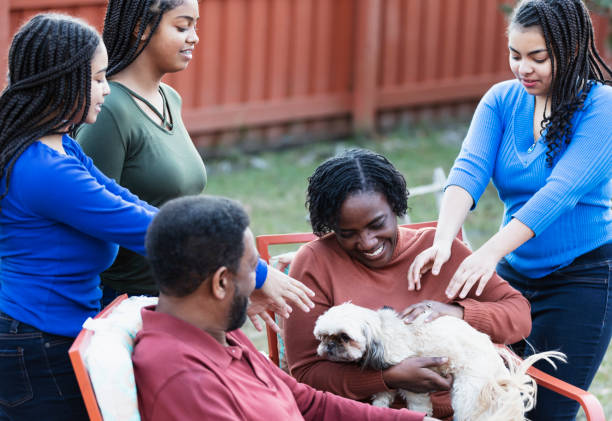 Family with three teenage girls and dog, in backyard An African-American family with three teenage girls together in their backyard, smiling. The parents, in their 50s, are sitting in chairs, and the daughters, 13, 14 and 16 years old, are standing around them. The mother has the family dog, a shih tzu, on her lap. small florida home stock pictures, royalty-free photos & images