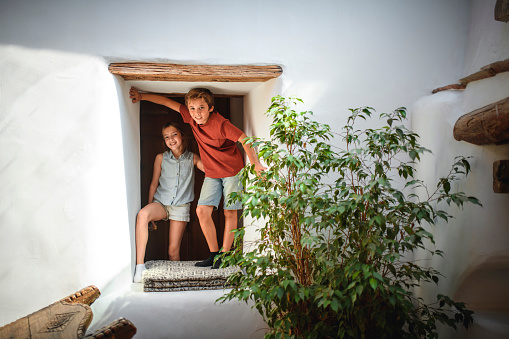 Young Spanish brother and sister standing in alcove of farmhouse family home and smiling at camera.