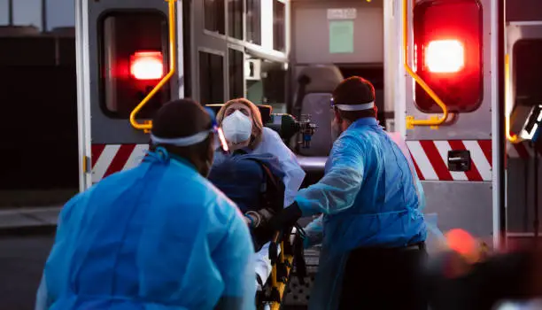 Photo of Paramedics loading patient into ambulance, wearing PPE