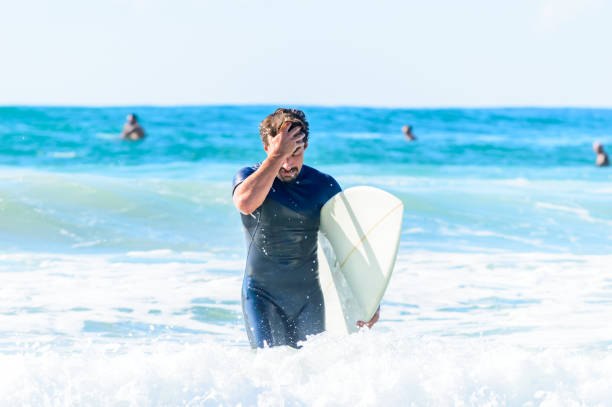 Smiling blonde man standing in the water with his blue surfboard