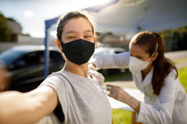 Teen girl taking a selfie while taking vaccine Teen girl taking a selfie while taking vaccine. vacina stock pictures, royalty-free photos & images