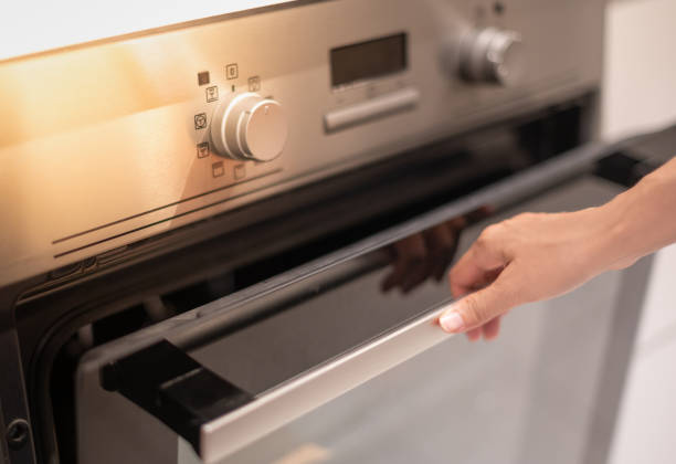 Female hand professional cook opening electric oven, while preparing dinner at home. Hobby, lifestyle. stock photo