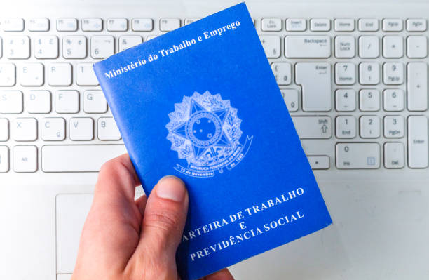 istock Young man holding a Brazilian work card over white laptop keyboard. Digital work document. 1311555661