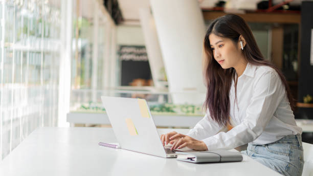 istock Young Asian students wearing headphones using their laptop in a coffee shop, writing notes on language learning, watching online webinars, audio listening courses, e-learning ideas. 1311560263