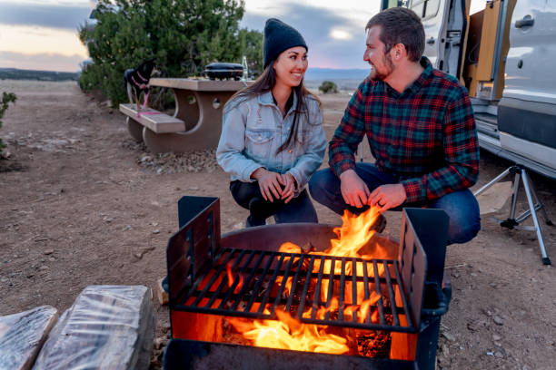 istock Young Multi-Ethnic Couple Kneeling To Warm Themselves By The Campfire, Smiling, Talking, Enjoying The Evening 1311565261