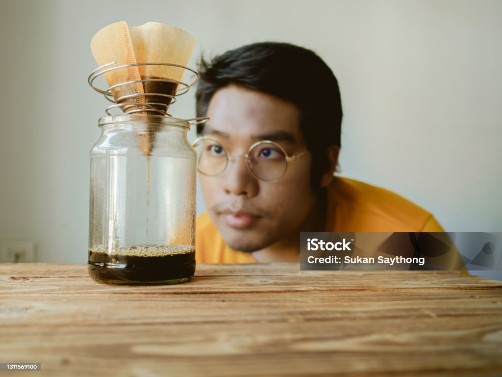 Drip brew by pouring hot water that has been filtered through roasted coffee beans contained in the filter.  man looking and observing the drip of coffee Brewery Stock Photo