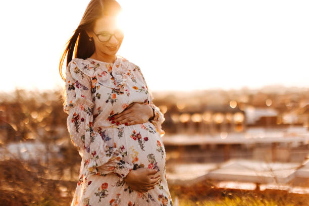 schwangere frauen genießen sonnenuntergang in der natur - magen fotos stock-fotos und bilder