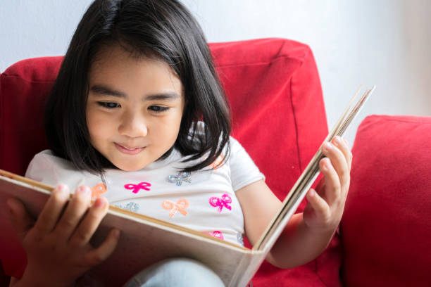 istock Little cute girl is reading a book hare sitting on a sofa 1311571800