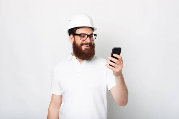 istock Photo of cheerful engineer man using smartphone and wearing hard hat 1311573623