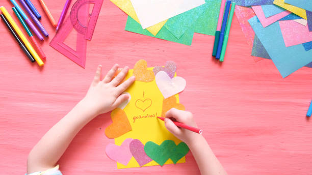 おばあちゃんのためのカードを作る小さな女の子。紙の装飾、多色のハートとカラフルなピンクの背景、 - oeuvre ストックフォトと画像