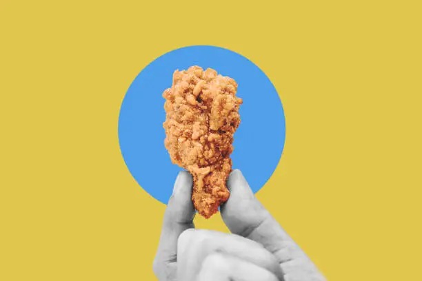 Photo of Hand holding fries chicken drumstick, on blue yellow background