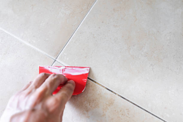 Floor tile fixing and renovation, Hand using trowel repairing old tile grout in bathroom stock photo