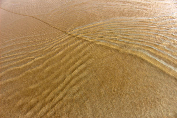 pequeñas olas hacen ondas en aguas poco profundas sobre la arena de la playa - poco profundo fotografías e imágenes de stock