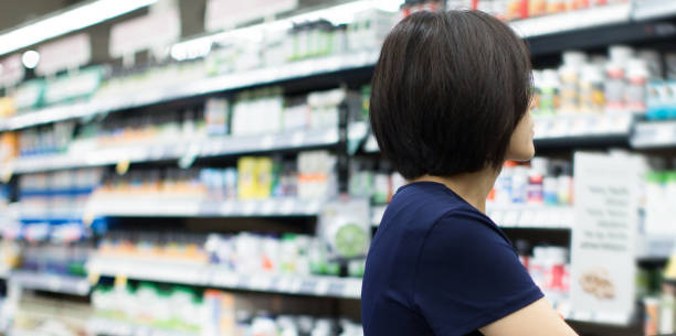 Woman Shopping at Grocery Market Pharmacy. Supermarket Shopper Doing Groceries. Female Holding Basket Trying to Decide which Products to Buy. Retail Healthcare Medicine, Vitamins, and Supplements. stock photo