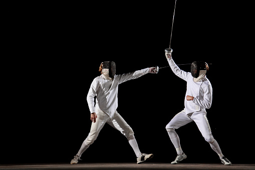 Two fencer in a fencing pose. One is attacking and one is defending. White on black background.