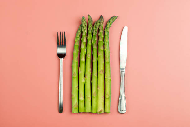 Asparagus with fork and knife on a pink background. Fresh vegetable asparagus for a healthy diet and nutrition. Vegetables and healthy food concept Asparagus with fork and knife on a pink background. Fresh vegetable asparagus for a healthy diet and nutrition. Vegetables and healthy food concept. High quality photo asparagus organic dinner close to stock pictures, royalty-free photos & images