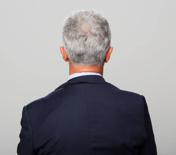 Rear view of mature man standing against grey background.