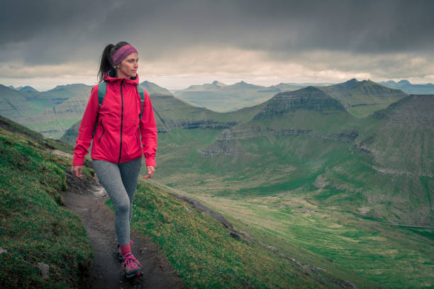 Woman hiking in mountain landscape on Eysturoy, Faroe Islands Young woman with purple jacket hiking in green mountain landscape on Eysturoy, Faroe Islands eysturoy photos stock pictures, royalty-free photos & images