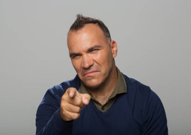 Portrait of angry mature man pointing index finger while standing against grey background.