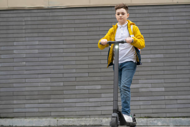 istock Modern teenager with backpack rides on electric scooter on brick wall background 1311594268
