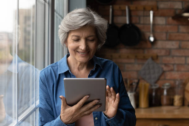 mujer latina de mediana edad sonriente usa tablet computer en la cocina - women book mature adult reading fotografías e imágenes de stock