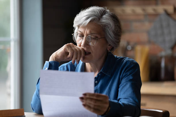 mujer latina mayor estresada recibe mala sorpresa leyendo carta oficial - note pad paper letter old fotografías e imágenes de stock