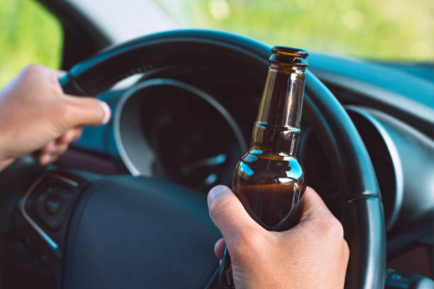 primer plano del conductor ebrio manos en el volante con una botella de cerveza. conducir bajo los efectos del alcohol - sólo hombres jóvenes fotografías e imágenes de stock