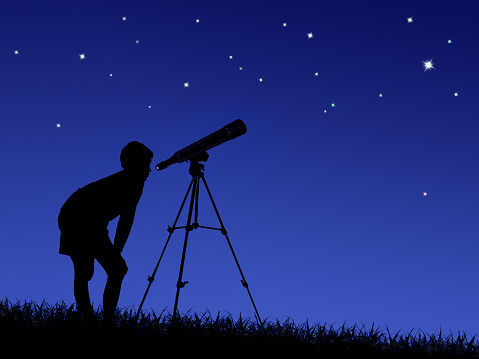 the boy looks at the stars through a telescope on the lawn