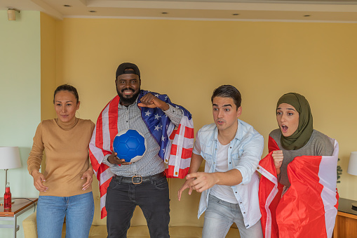 Group of Multicultural Friends is Following a Sports Event on Television in Comfortable Apartment and Support Their Teams from the USA and Canada.