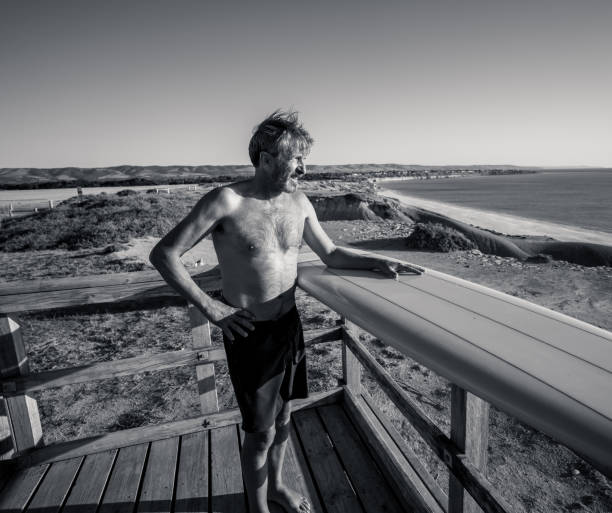 surfer mûr attirant d’homme avec la planche de surf vintage fraîche sur la plage au coucher du soleil. adulte aîné heureux d’être de retour pour surfer. aventure sportive en plein air, personnes âgées actives et mode de vie à la retraite. - senior adult surfing aging process sport photos et images de collection