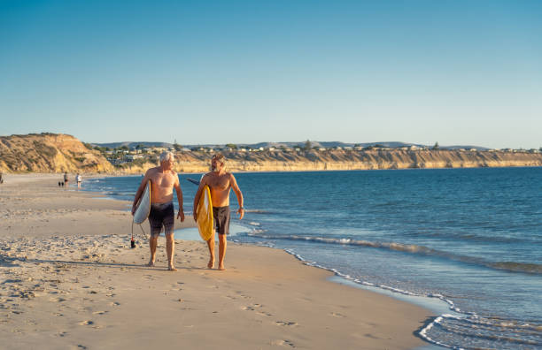 deux hommes mûrs marchant avec des planches de surf sur la belle plage appréciant le paradis et le mode de vie de retraite. attrayant ajustement amis adultes seniors ayant du plaisir à surfer. chez les personnes actives et en bonne santé. - senior adult surfing aging process sport photos et images de collection