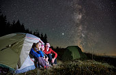 Travelers sitting in camp tent under night starry sky.