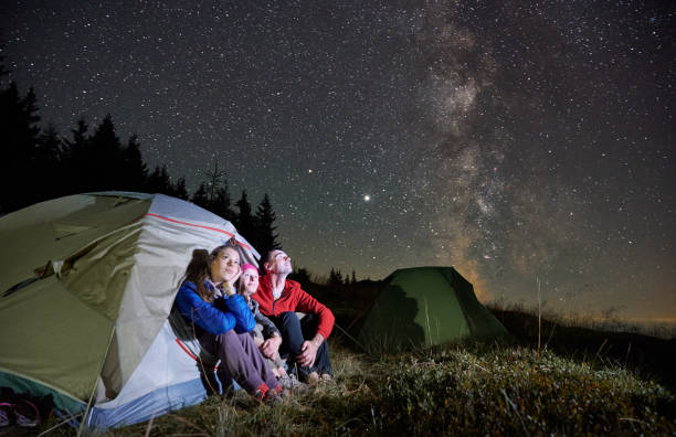 Travelers sitting in camp tent under night starry sky. Family hikers sitting in tourist tent under beautiful night sky with stars. Travelers resting in camp tent and looking at magical starry sky with Milky Way. Night camping in the mountains. astronomy stock pictures, royalty-free photos & images