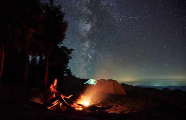 istock Female hiker sitting near campfire under night starry sky. 1311601443