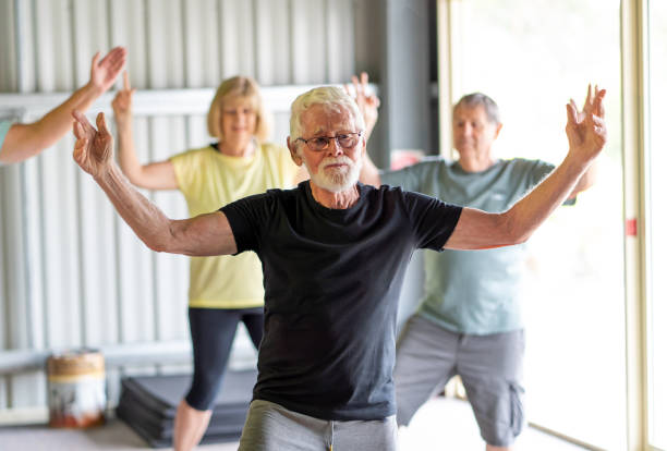 groupe de personnes âgées dans la classe de tai chi exerçant dans un mode de vie actif de retraite. avantages pour la santé mentale et physique de l’exercice et de la condition physique chez les personnes âgées. concept de soins de santé et de bie - tai chi photos et images de collection