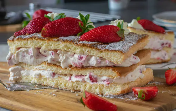 homemade creamcake with strawberries made with biscuit dough and whipped cream filling. Served on a wooden board on kitchen table. Ready to eat