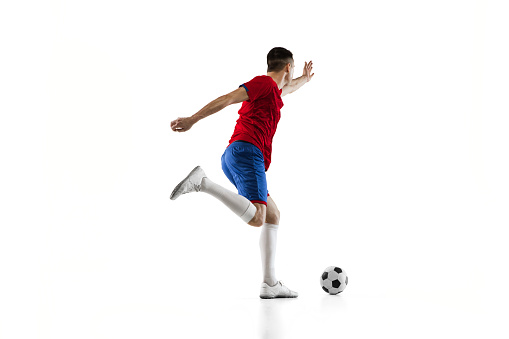 Kick the ball. Young Caucasian man, male soccer football player in red blue uniform isolated on white background. Action, dynamic. Concept of active life, team game, energy, sport. Copy space for ad.