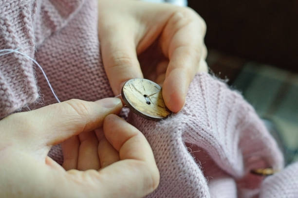 female workers' hands sew a wooden button to a jacket. close-up.
