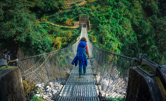 Mujer joven cruzando puente colgante en el campo base del Annapurna, Nepal photo