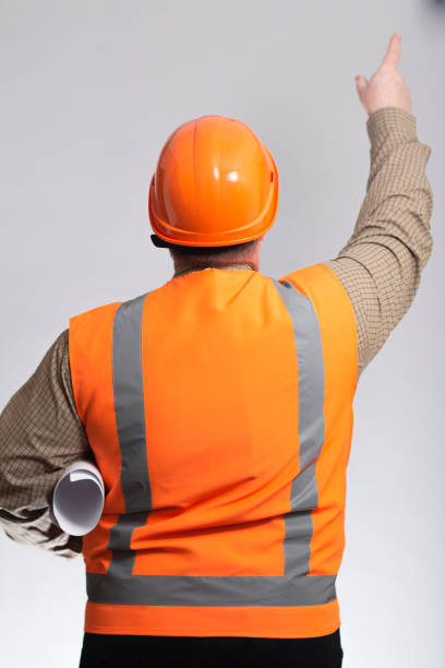 istock back of plupm construction worker in hard hat and reflective vest on studio background showing with hand direction forward, foreman with project under arm 1311622669