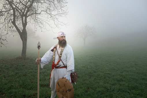 Man is standing in traditional japanese shugendo outfit on green meadow in heavy fog