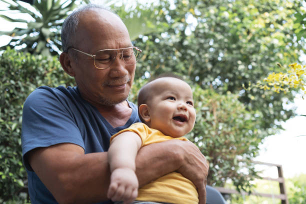 szczęśliwy azjatycki dziadek obejmując lub trzymając swojego małego wnuka na świeżym powietrzu. - asian ethnicity male park men zdjęcia i obrazy z banku zdjęć