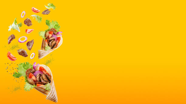 Two doner kebab or shawarma with ingredients floating in the air: beef meat, lettuce, onion, tomatos, spice. Yellow orange background. Copy space. Two doner kebab or shawarma with ingredients floating in the air: beef meat, lettuce, onion, tomatos, spice. Yellow orange background. Copy space. burrito photos stock pictures, royalty-free photos & images