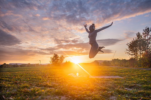 Happy woman jumping on exercising mat at sunset